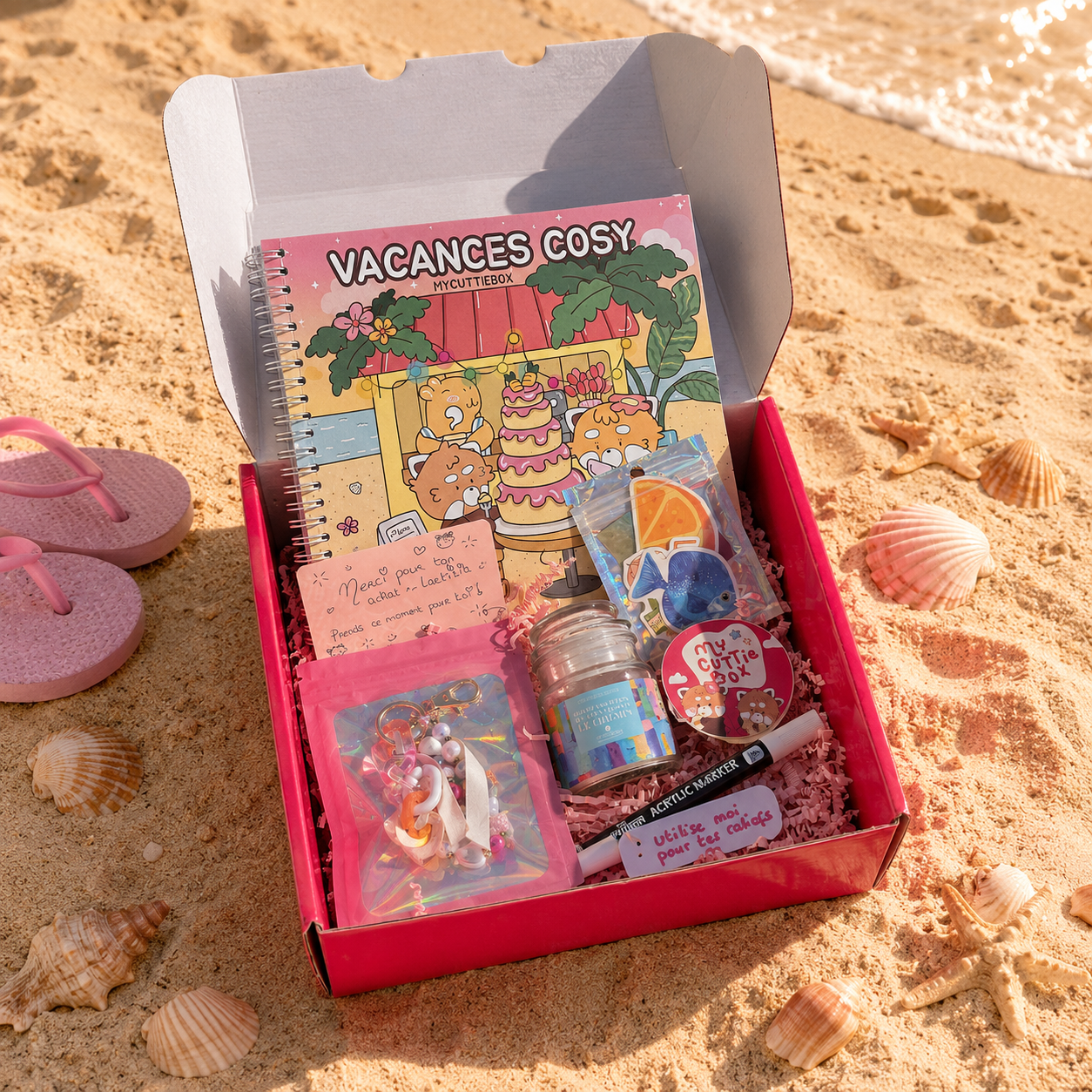 Box MyCuttieBox Vacances Cosy posée sur le sable avec accessoires de plage